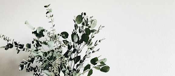 A wooden table with a vase of flowers, a clock, and a roll of tape on it.
