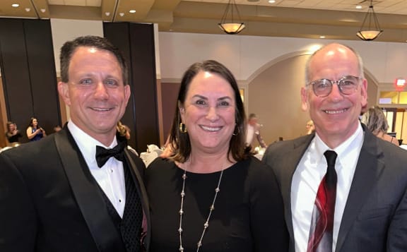 a man in a tuxedo and a woman in a black dress and a man in a gray suit