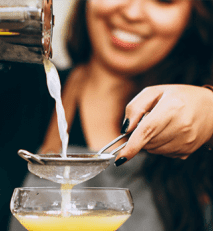 a woman pouring orange juice into a cocktail