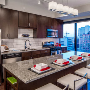 A large kitchen with stainless steel appliances, spacious marble countertops, and large wooden cabinets at NIC on 5th Apartments. 