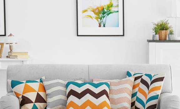 A white couch with colorful pillows in front of a white wall with framed pictures.