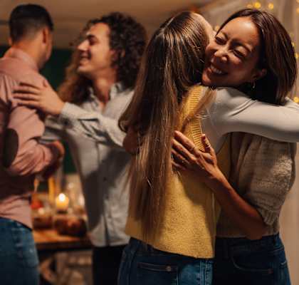 Three people hug each other in a room with lights.