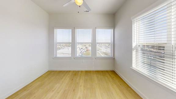 A room with a ceiling fan and two windows.