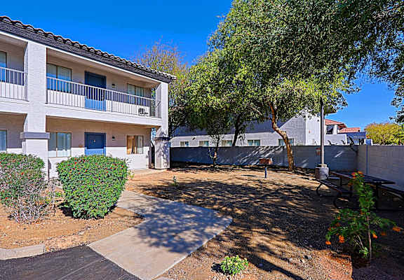 a courtyard with a tree in front of a white apartment building