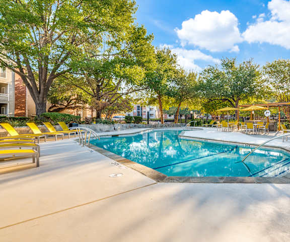 A swimming pool surrounded by yellow chairs and trees.