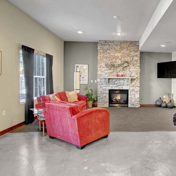 The common area at Allegro with a fireplace, couch, chairs, a TV, and a piano. 