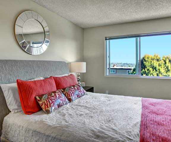 A bedroom with a queen-size bed with a colorful bedspread, a dresser, decorations, window, and nightstands at Overlook on Magnolia Apartments. 