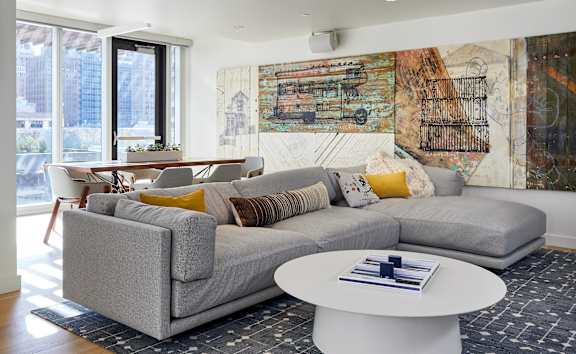 A living room with a grey couch and a large abstract painting on the wall.