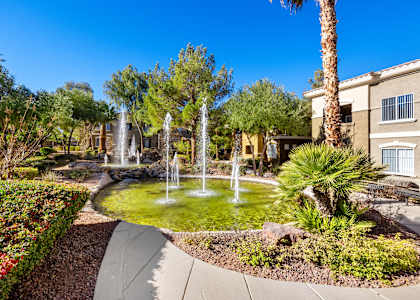 A garden with a fountain in the middle of a grassy area.