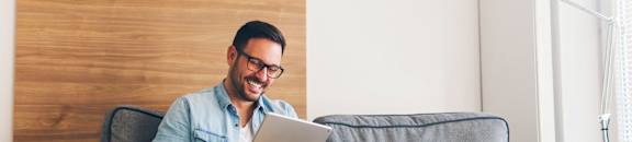 A man is sitting on a grey couch using a tablet.