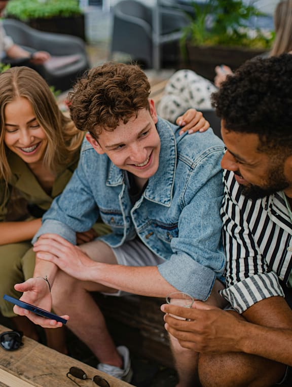 A group of friends are sitting together, one of them is holding a smartphone.