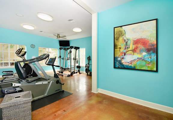 A gym with a treadmill, elliptical machines, and a painting on the wall.