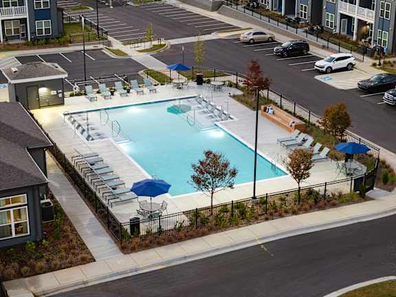 A swimming pool surrounded by chairs and umbrellas in a parking lot.