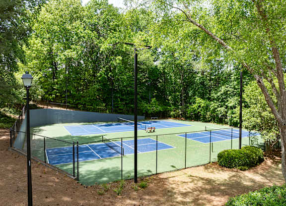 A tennis court surrounded by trees and a lamp post.