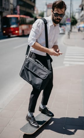 a man on a skateboard carrying a bag and looking at his phone