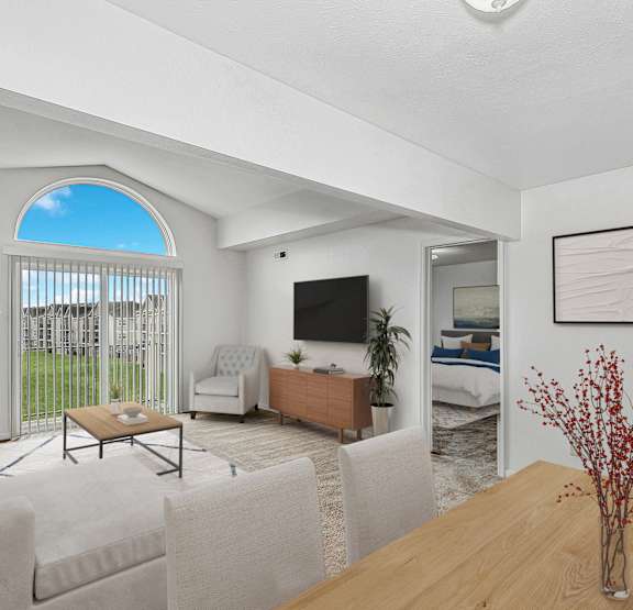 A living room with a television, a sofa, a chair, a coffee table, and a bed in the background at Orchard Lakes Apartments in Toledo, OH