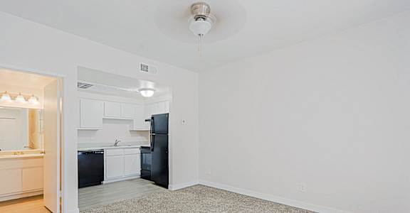 an empty living room with a kitchen in the background