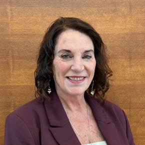 A woman with dark brown hair wearing a purple blazer.
