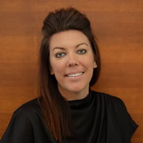 A woman with long brown hair and a blue shirt is smiling.