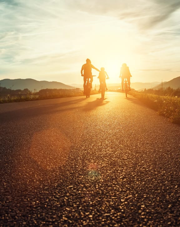 a group of people riding bikes on an empty road at sunset