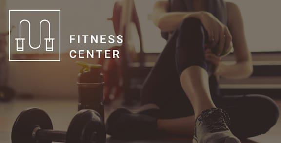 A woman is sitting on the floor in a fitness center, surrounded by dumbbells and a water bottle at Adler Montford Park + Drexel Townes, Charlotte, NC, 28209.