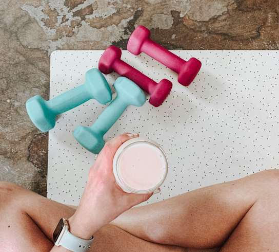 A person is holding a glass of milk and lifting two dumbbells.