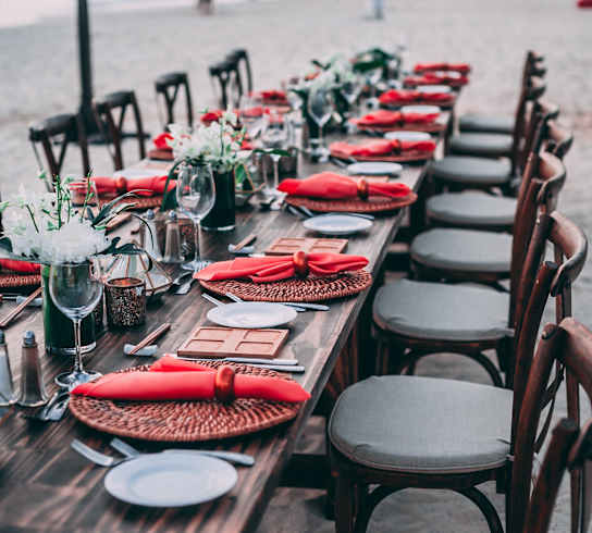 a long wooden table with red napkins and chairs at the beach