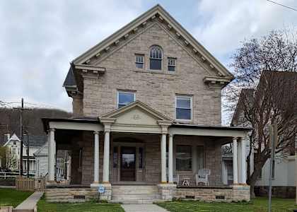 a stone house with a porch and a tree in front of it