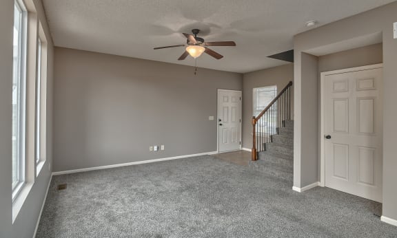 an empty living room with a ceiling fan and a staircase