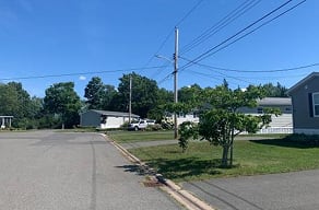 A road with a white car and a grey house on the side.