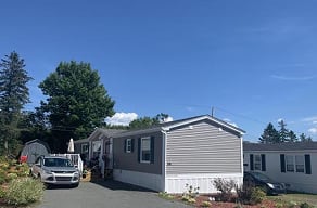 A silver car is parked in front of a grey house.