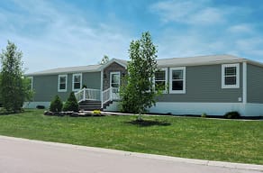 A green manufactured home with trees in it's yard