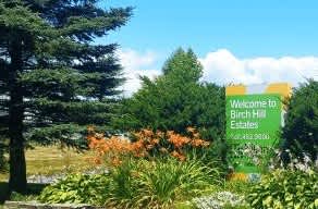 A sign welcoming people to Birch Hill Estates stands in front of a green lawn.