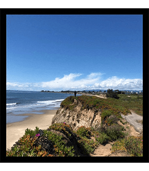 a view of the beach and a person standing on a cliff