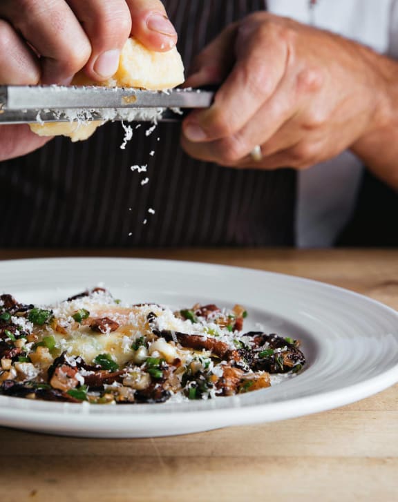 a person sprinkling cheese on a plate of food