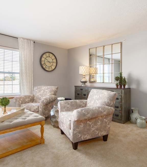 A living room with a white couch, a patterned chair, and a wooden coffee table.