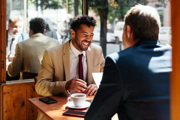 a man in a suit sitting at a table with a cup of coffee