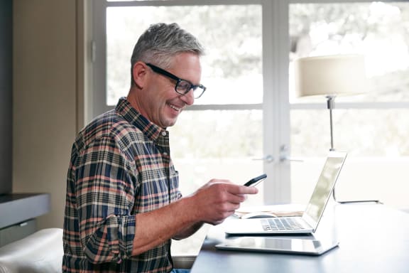 a man sitting in front of a laptop computer and holding a cell phone