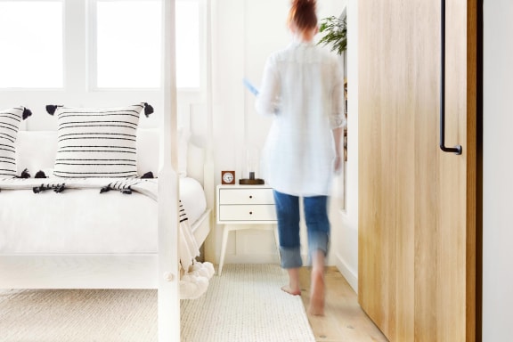 a woman walking into a bedroom with a bed and a nightstand