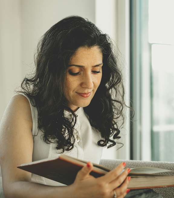 A woman is reading a book with a white shirt and dark hair.