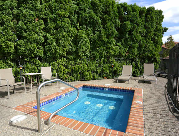 A small pool surrounded by a brick border and a table and chairs.