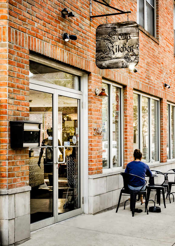 A man in a blue shirt is sitting at a table outside a brick building with a sign that reads "Hofbrau".