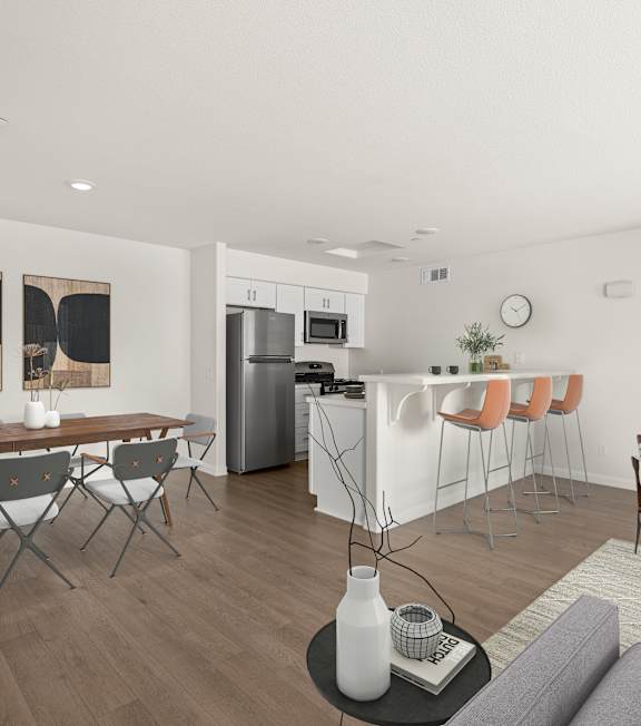 A modern living room with a grey sofa, wooden floors, and a white kitchen area.