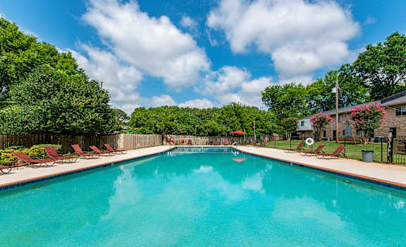 A large swimming pool surrounded by trees and lawn chairs.
