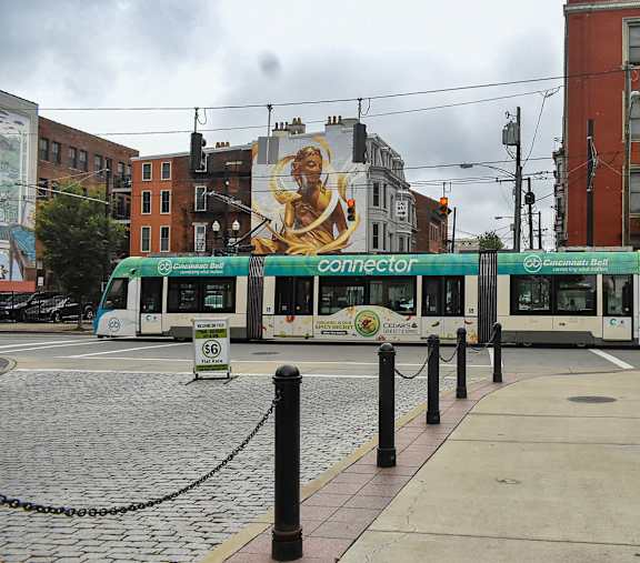 A green and white tram is parked on a cobblestone street.