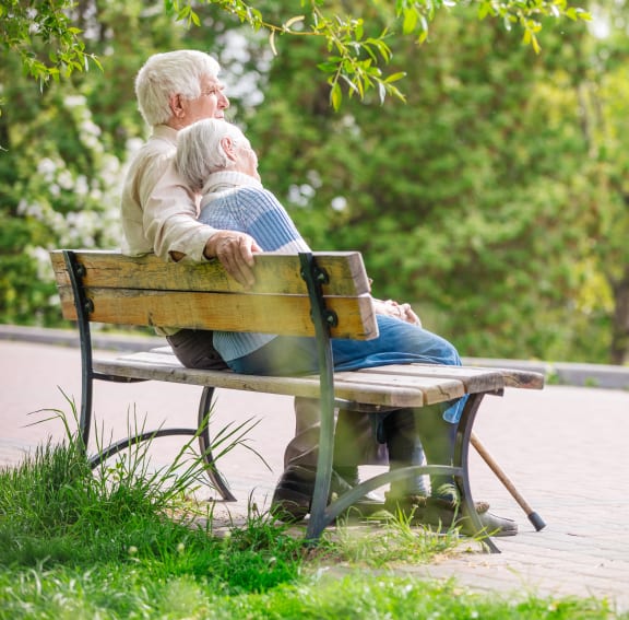 An senior couple sitting together on a bench in a park.