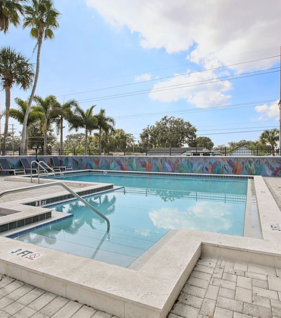 A pool surrounded by palm trees and a fence.