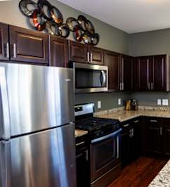 A kitchen with a granite counter top and dark brown cabinets.