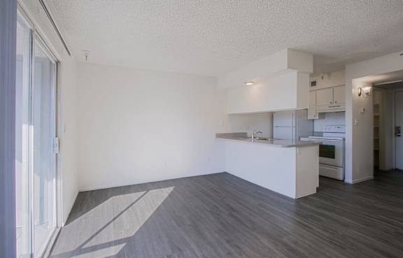 the living room and kitchen of an apartment with white walls and wood flooring