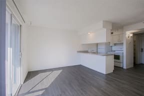 the living room and kitchen of an apartment with white walls and wood flooring